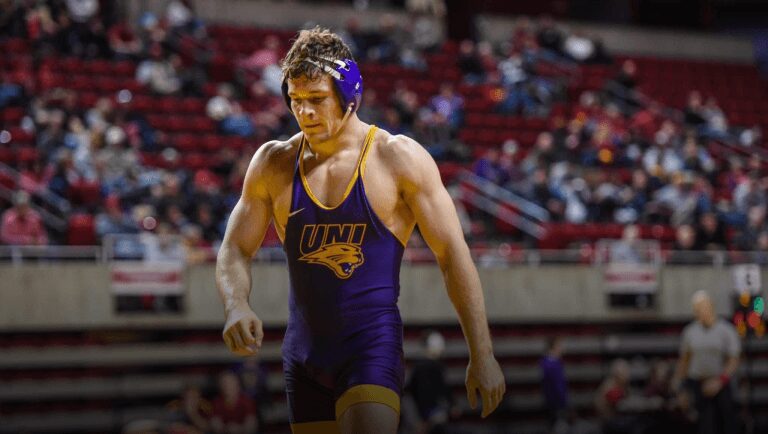 A man in purple wrestling uniform standing on the ground.